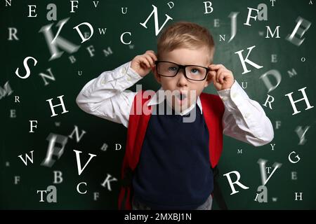 Lustiges kleines Kind mit Brille und Buchstaben in der Nähe der Tafel. Sprachtherapiekonzept Stockfoto