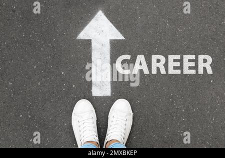 Eine Frau, die neben einem Pfeil auf Asphalt steht, Draufsicht. Career-Choice-Konzept Stockfoto