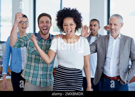 Ein weiterer Sieg für das Team. Eine Gruppe glücklicher Kollegen, die im Büro stehen. Stockfoto