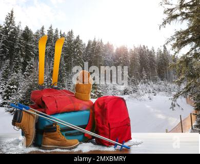 Koffer mit warmer Kleidung auf Holzfläche vor wunderschöner Winterlandschaft Stockfoto