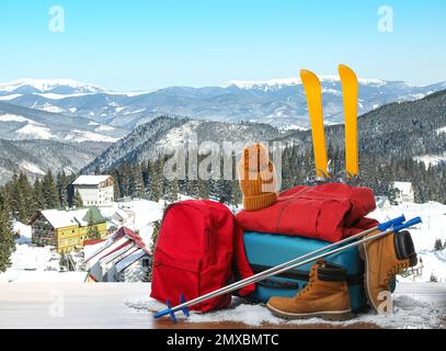 Koffer mit warmer Kleidung auf Holzfläche vor einer wunderschönen Berglandschaft Stockfoto