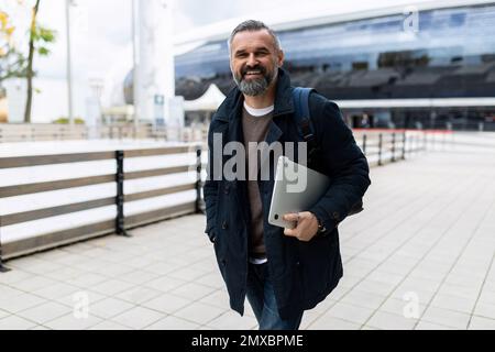 Reifer bärtiger Mann mit Laptop, der draußen herumläuft Stockfoto