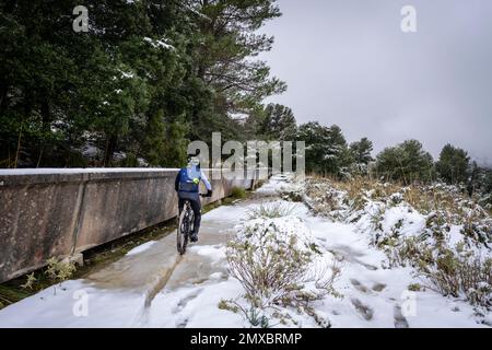 Radfahrer im Schnee neben dem Wasserkanal, dem Gorg Blau Reservoir, Escorca, Mallorca, Balearen, Spanien Stockfoto