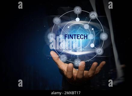 FinTech-Konzept. Ein Mann, der verschiedene Symbole auf dunkelblauem Hintergrund zeigt, Nahaufnahme Stockfoto