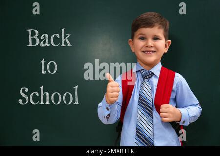 Süßes kleines Kind in der Nähe der Tafel mit Phrase ZURÜCK ZUR SCHULE Stockfoto