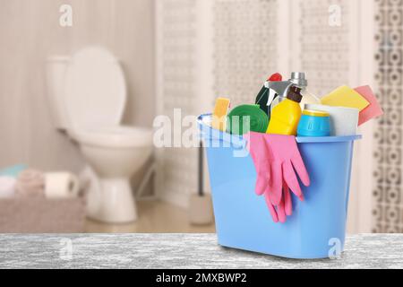 Eimer mit Reinigungsutensilien auf grauem Steintisch im Badezimmer, Platz für Text Stockfoto