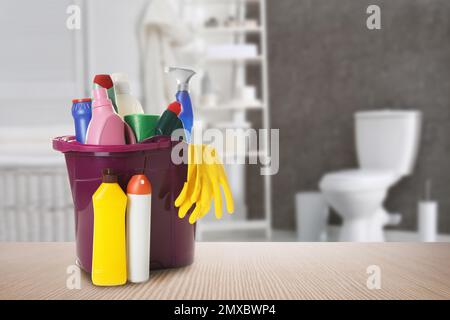 Eimer mit Reinigungsmitteln auf Holztisch im Badezimmer, Platz für Text Stockfoto