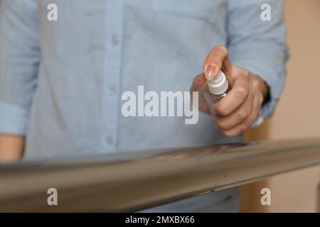 Frau, die Antiseptikum auf Metallgeländer spritzt, drinnen, Nahaufnahme Stockfoto