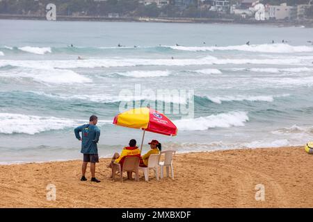 An einem Sommertag im North Steynebeach, Manly, Sydney, Australien, sitzen australische Surfer unter einem Regenschirm Stockfoto