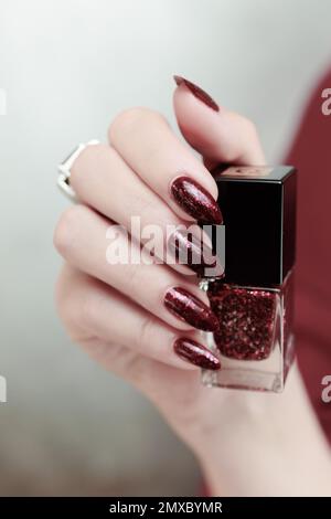 Frau Hand mit langen Nägeln und eine Flasche dunkel Nagellack rot burgunderrot Stockfoto