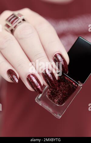 Frau Hand mit langen Nägeln und eine Flasche dunkel Nagellack rot burgunderrot Stockfoto