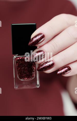 Frau Hand mit langen Nägeln und eine Flasche dunkel Nagellack rot burgunderrot Stockfoto