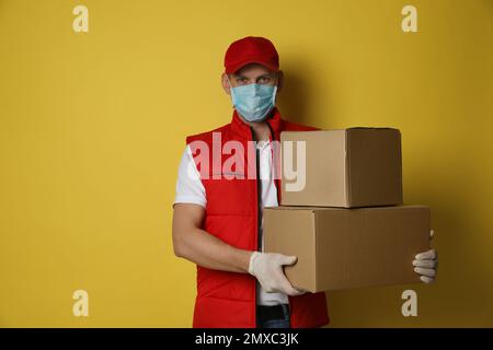 Kurier in Schutzmaske und Handschuhen mit Kartons auf gelbem Hintergrund. Zustelldienst während der Coronavirus-Quarantäne Stockfoto