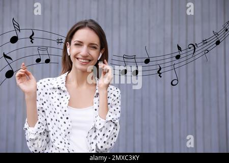 Junge Frau, die mit kabellosen Kopfhörern in der Nähe der grauen Wand Musik hört Stockfoto
