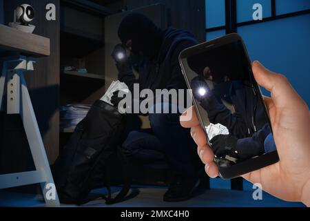 Ein Mann beobachtet die Situation in seinem Haus mit der CCTV-App auf dem Smartphone, Nahaufnahme. Ein Dieb, der Geld stiehlt Stockfoto