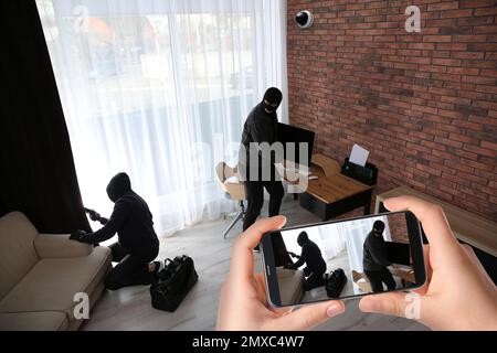 Ein Mann beobachtet die Situation in seinem Haus mit der CCTV-App auf dem Smartphone, Nahaufnahme. Diebe stehlen Computer Stockfoto