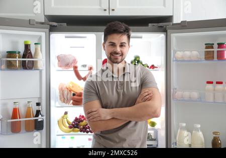 Junger Mann in der Nähe eines offenen Kühlschranks in der Küche Stockfoto
