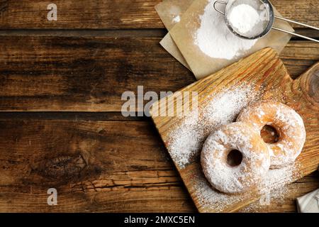 Köstliche Donuts mit Puderzucker auf Holztisch, flach liegend. Platz für Text Stockfoto