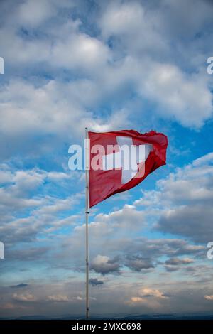 Die Schweizer Flagge bläst im Wind, der Hintergrund ist bewölkt Stockfoto