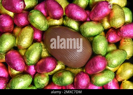 Ein Stapel mehrfarbiger und in verschiedenen Größen verpackter Schokoladeneier in Pink, Rot, Gelb und Limettengrün mit einem Ei. Stockfoto