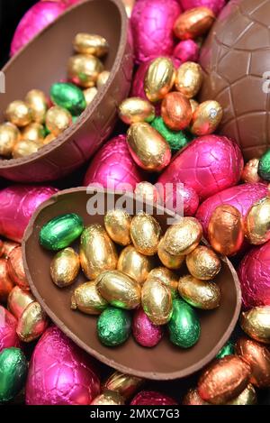 Ein Stapel bunter und in verschiedenen Größen mit bunten Folien verpackter Schokoladeneier in Pink, Rot, Gold und Limettengrün. Stockfoto