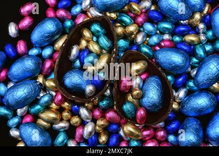 Ein Haufen mehrfarbiger und in verschiedenen Größen verpackter Schokoladeneier in Blau, Pink, Silber und Gold. Stockfoto