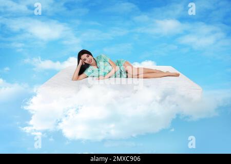 Junge Frau, die auf einer Matratze in Wolken liegt Stockfoto