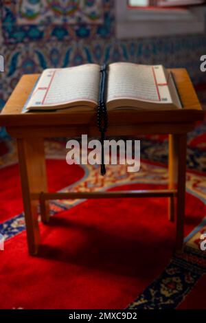 Der Heilige Koran auf dem Rednerpult mit einem Rosenkranz oder Gebetsperlen in der Moschee. Ramadan oder islamisches vertikales Hintergrundbild. Selektiver Fokus. Stockfoto