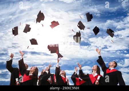 Glückliche Studenten mit Diplomen, die ihre Abschlussmützen draußen in die Luft werfen Stockfoto