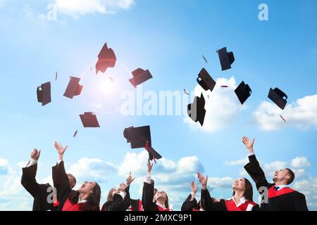 Glückliche Schüler, die ihre Abschlussmützen draußen in die Luft werfen Stockfoto