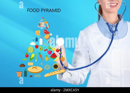 Ernährungswissenschaftler und Lebensmittelpyramide auf hellblauem Hintergrund, Nahaufnahme Stockfoto