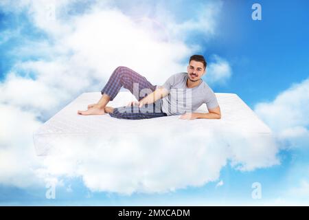 Junger Mann, der auf einer Matratze in Wolken liegt Stockfoto