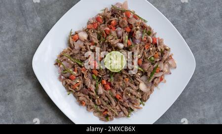 Huhn oder Rindfleisch mit traditionellem indonesischen Sambal. Zwiebeln, Chilis, Kokosöl, Limettenblätter, Salz. Serviert auf einem weißen Teller und einem Steinsockel. Stockfoto