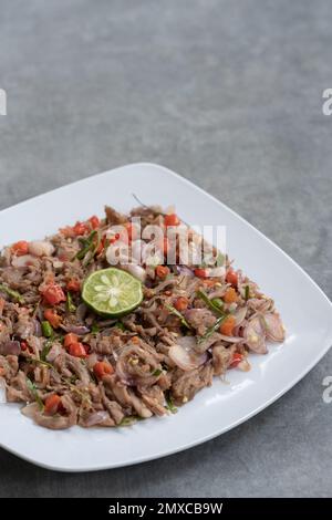 Huhn oder Rindfleisch mit traditionellem indonesischen Sambal. Zwiebeln, Chilis, Kokosöl, Limettenblätter, Salz. Serviert auf einem weißen Teller und einem Steinsockel. Stockfoto