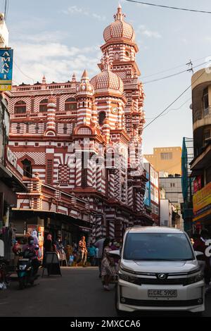 Colombo, Sri Lanka - 3. Dezember 2021: Vertikales Straßenfoto mit der Jami UL-Alfar-Moschee, auch bekannt als Rote Moschee. Normale Menschen und Autos sind auf dem Zug Stockfoto