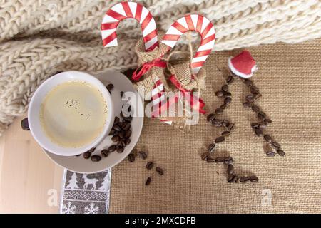 Weihnachtstisch mit einer Tasse Kaffee, zwei dekorativen Zuckerstangen und einem Weihnachtsbaum aus Kaffeebohnen mit einem kleinen Weihnachtsmannmütze. Oben Stockfoto
