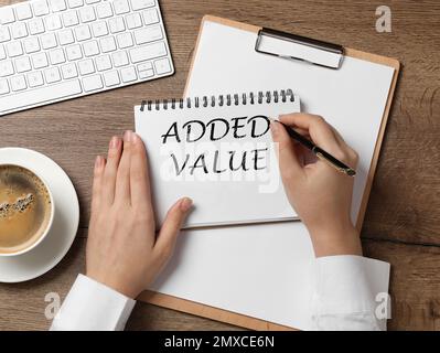 Mehrwert-Konzept. Draufsicht einer jungen Frau, die auf einem Holztisch in Notizbuch schreibt Stockfoto