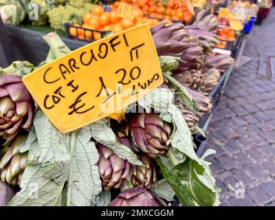 Markt, italienisches Preisschild für frische Artischocken mit selektivem Fokus auf einem offenen Bauernmarkt in Italien. Frische und reife Artischocke auf Gemüseständen oder Stockfoto