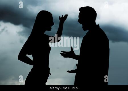 Silhouetten eines streitenden Paares gegen den Himmel mit schweren Regenwolken. Beziehungsprobleme Stockfoto