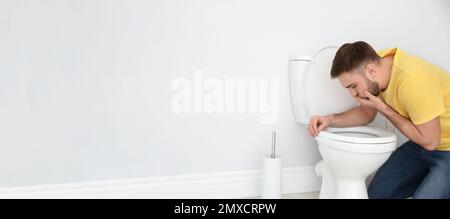 Junger Mann mit Übelkeit über Toilettenschüssel in Innenräumen, Platz für Text. Bannerdesign Stockfoto