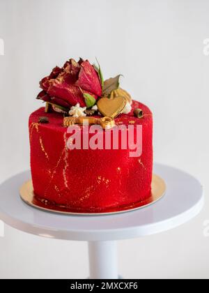 Mattierter roter Samtkuchen mit Blumen- und Herzauflagen und goldenen Strichen auf weißem Studiohintergrund Stockfoto