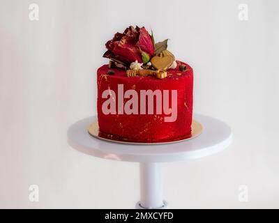 Mattierter roter Samtkuchen mit Blumen- und Herzauflagen und goldenen Strichen auf weißem Studiohintergrund Stockfoto