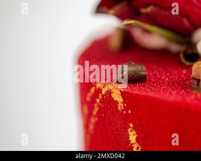 Mattierter roter Samtkuchen mit Blumen- und Herzauflagen und goldenen Strichen auf weißem Studiohintergrund Stockfoto