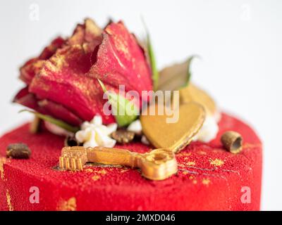 Mattierter roter Samtkuchen mit Blumen- und Herzauflagen und goldenen Strichen auf weißem Studiohintergrund Stockfoto