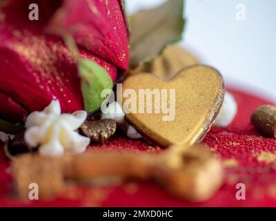 Mattierter roter Samtkuchen mit Blumen- und Herzauflagen und goldenen Strichen auf weißem Studiohintergrund Stockfoto