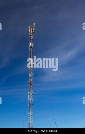 Telekommunikationsturm mit Radio, Mikrowelle und TV-Antennensystem im Wald vor dem blauen Himmel. Antennenturm, Ansicht vom g Stockfoto