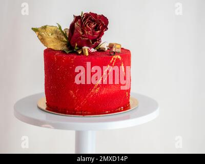 Mattierter roter Samtkuchen mit Blumen- und Herzauflagen und goldenen Strichen auf weißem Studiohintergrund Stockfoto