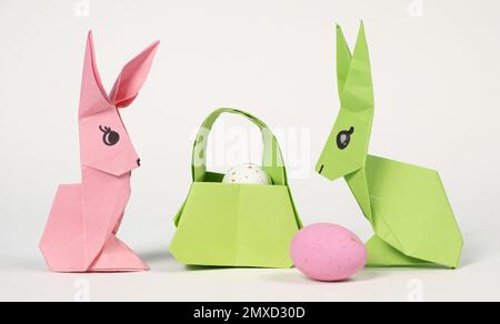 Ostern-Origami-Häschen und ein Korb Eier auf weißem Hintergrund. Papierhandwerk, machen Sie es selbst. Stockfoto