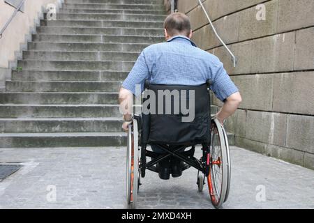 Rollstuhlfahrer, der vor einer nicht barrierefreien Außentreppe steht, Rückansicht Stockfoto