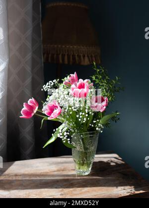 Wunderschöner Strauß von Tulpen in Glasvase auf weißem Marmortisch. Platz für Text. Stockfoto